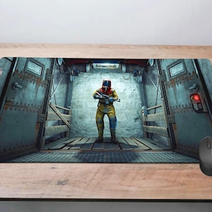 May include: Rectangular mousepad featuring a person in a yellow hazmat suit holding a rifle, standing in a metal corridor. The image has a post-apocalyptic theme. A black wireless mouse is on the right side of the mousepad.