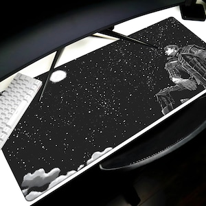 Puede incluir: Alfombrilla de escritorio en blanco y negro con una ilustración de estilo manga de un personaje contra un cielo estrellado. El diseño incluye una luna llena y detalles de nubes. Se ven un teclado blanco y un monitor negro.