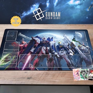 May include: A Gundam card game playmat featuring multiple mecha robots in a space scene. The mat has designated zones for gameplay and the text "ZONES OR NO ZONES". Several Gundam card game cards are visible.