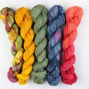 May include: Five skeins of colorful yarn in a row. The yarn colors include a mix of yellow, green, blue, and red hues. The yarn is twisted and appears soft, perfect for knitting or crocheting projects.