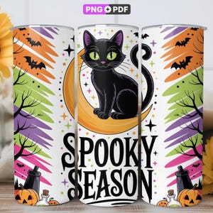 May include: A cylindrical tumbler featuring a black cat sitting on a yellow crescent moon, surrounded by bats, bare trees, and colorful brushstrokes. The text "SPOOKY SEASON" is printed in large black letters. The design includes small stars and pumpkins.