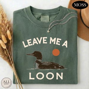 A green t-shirt with a graphic design of a duck and the text "LEAVE ME A LON" printed on it.