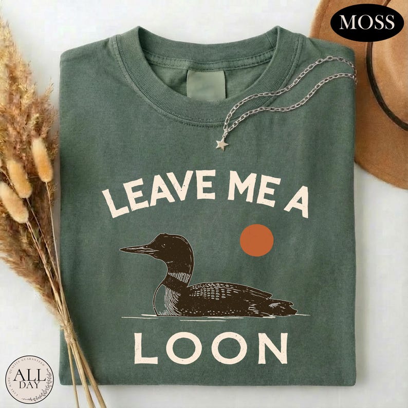 A green t-shirt with a graphic design of a duck and the text "LEAVE ME A LON" printed on it.