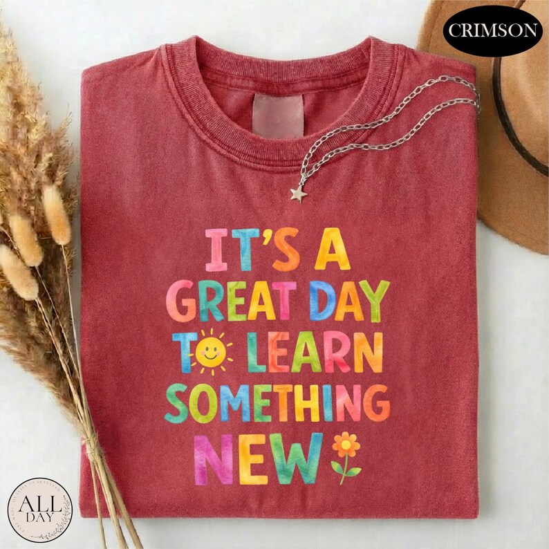 A red t-shirt with the text "IT'S A GREAT DAY TO LEARN SOMETHING NEW" printed on it, along with a flower and a star charm.