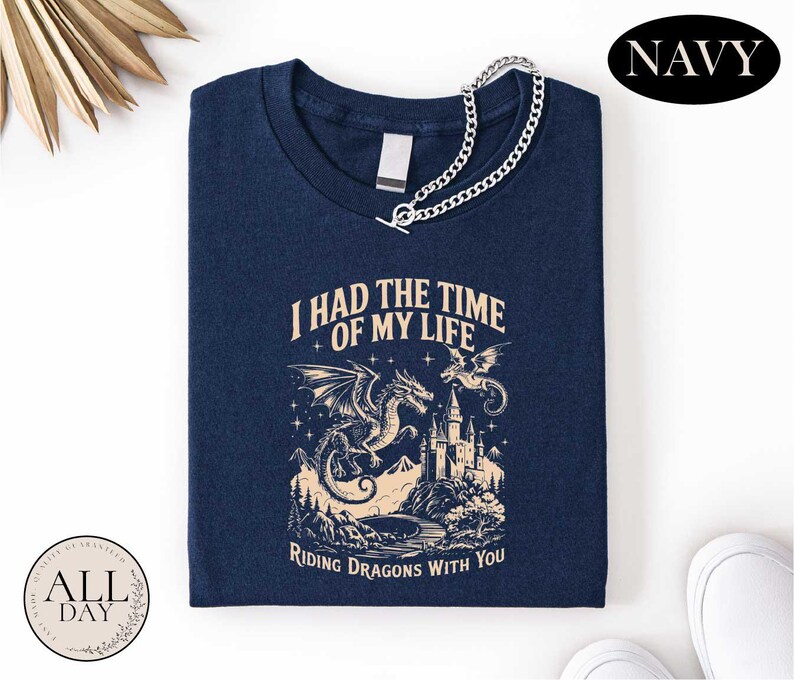 a navy blue t-shirt with a graphic design depicting a castle, a dragon, and mountains, along with the text "I HAD THE TIME OF MY LIFE" and "RIDING DRAGONSLIES WITH YOU".