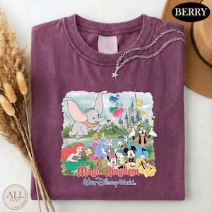 A purple t-shirt with a Disney-themed graphic design, including characters from the Disney film "Magic Kingdom" and a castle in the background.
