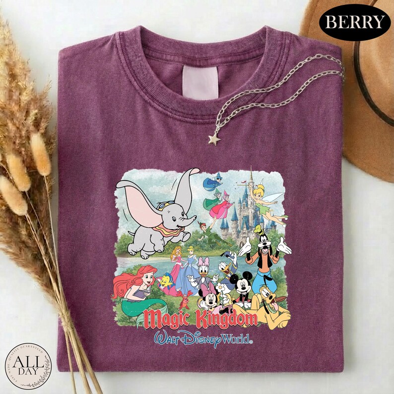 A purple t-shirt with a Disney-themed graphic design, including characters from the Disney film "Magic Kingdom" and a castle in the background.