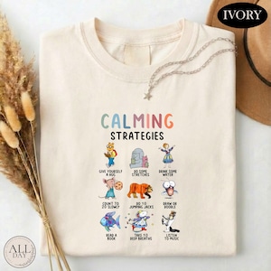 a white t-shirt with a colorful graphic design depicting various calming strategies, such as giving oneself a hug, doing some stretches, drinking water, reading a book, and listening to music.