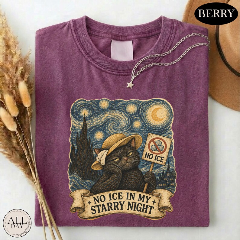 May include: A berry-colored t-shirt featuring a graphic of a black cat wearing a straw hat against a swirling starry night sky. The cat holds a sign with a no-ice symbol and the text NO ICE IN MY STARRY NIGHT printed on a banner below.
