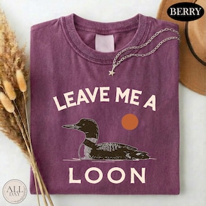 a purple t-shirt with a graphic design of a duck and the text "LEAVE ME A LON" printed on it.