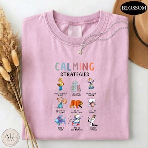 A pink t-shirt with a graphic design of various calming strategies and illustrations, including a bear, a bird, a cat, and other animals.