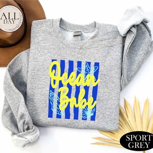 a gray sweatshirt with a blue and yellow graphic design, a brown hat, and some yellow leaves, all placed on a white background.