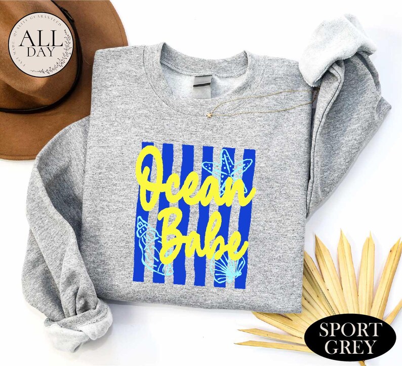 a gray sweatshirt with a blue and yellow graphic design, a brown hat, and some yellow leaves, all placed on a white background.
