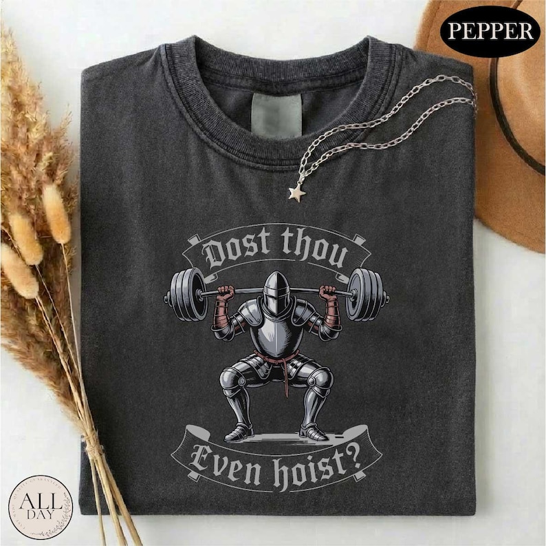 a black t-shirt with a graphic design depicting a knight lifting a barbell, accompanied by the text "Do you even hoist?"