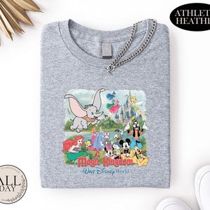 A gray t-shirt with a graphic design featuring various Disney characters and the text "Magic Kingdom" and "Woo Disney World" printed on it.