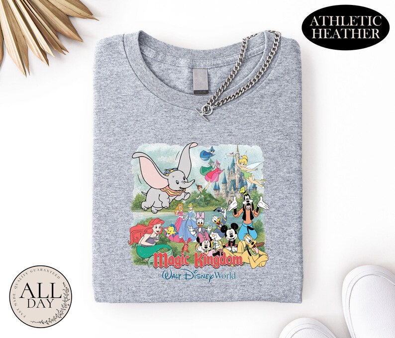 A gray t-shirt with a graphic design featuring various Disney characters and the text "Magic Kingdom" and "Woo Disney World" printed on it.