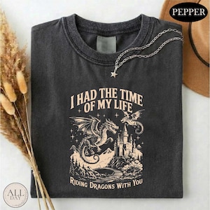 a black t-shirt with a graphic design depicting a castle, a dragon, and mountains, along with the text "I HAD THE TIME OF MY LIFE RIDING DRagons WITH YOU".