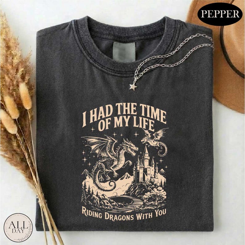 a black t-shirt with a graphic design depicting a castle, a dragon, and mountains, along with the text "I HAD THE TIME OF MY LIFE RIDING DRagons WITH YOU".