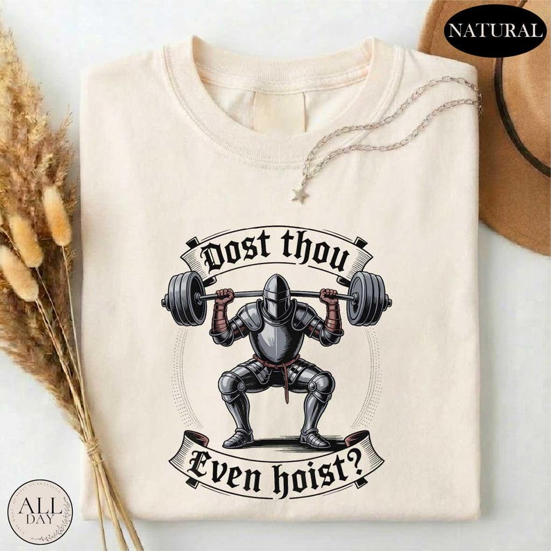 a white t-shirt with a graphic design depicting a knight lifting a barbell, accompanied by the text "Dost thou even hoist?"