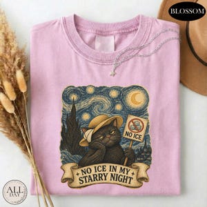 May include: A light pink t-shirt featuring a graphic of a black cat wearing a straw hat against a swirling blue starry night background. The cat holds a sign with a crossed-out ice cube icon and the text NO ICE. Below, a banner reads NO ICE IN MY STARRY NIGHT.