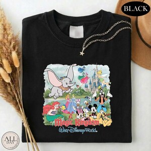 A black t-shirt with a colorful graphic of Disney characters from the Magic Kingdom, including Dumbo, Minnie Mouse, Donald Duck, and other iconic figures, along with the text "Magic Kingdom Walt Disney World."