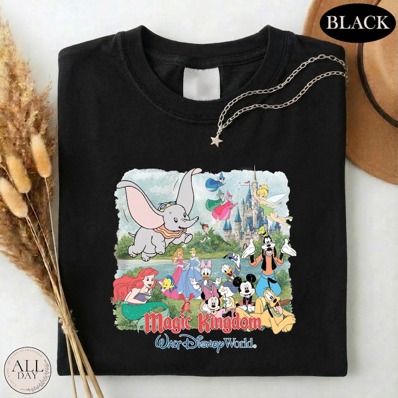 A black t-shirt with a colorful graphic of Disney characters from the Magic Kingdom, including Dumbo, Minnie Mouse, Donald Duck, and other iconic figures, along with the text "Magic Kingdom Walt Disney World."