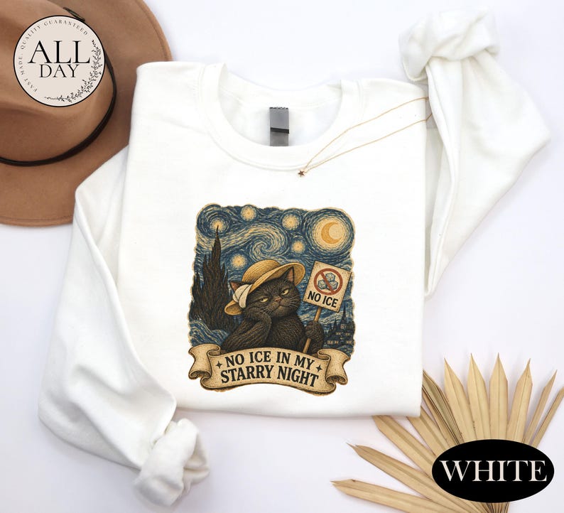 May include: A white long-sleeve sweatshirt featuring a graphic of a black cat wearing a hat, set against a swirling starry night background. The cat holds a sign that says NO ICE and a banner below reads NO ICE IN MY STARRY NIGHT.