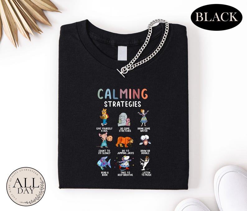a black t-shirt with a colorful graphic design of various cartoon characters and text, along with a chain.