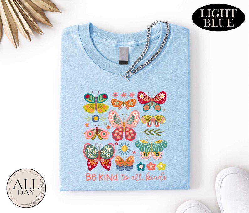 A light blue t-shirt with a colorful butterfly design and the text "Be Kind to all kinds" printed on it.