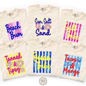 a collection of six beige t-shirts with colorful text and designs printed on them.