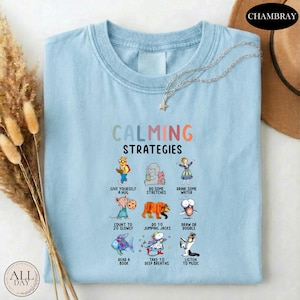 A light blue t-shirt with a colorful graphic design depicting various calming strategies, such as giving oneself a hug, drinking water, and reading a book.