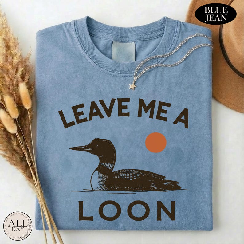 A blue t-shirt with a graphic design of a duck and the text "LEAVE ME A LON" printed on it.