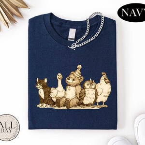 A navy blue t-shirt with a graphic design depicting a group of animals, including a bear, cat, duck, chicken, and owl, all wearing party hats.