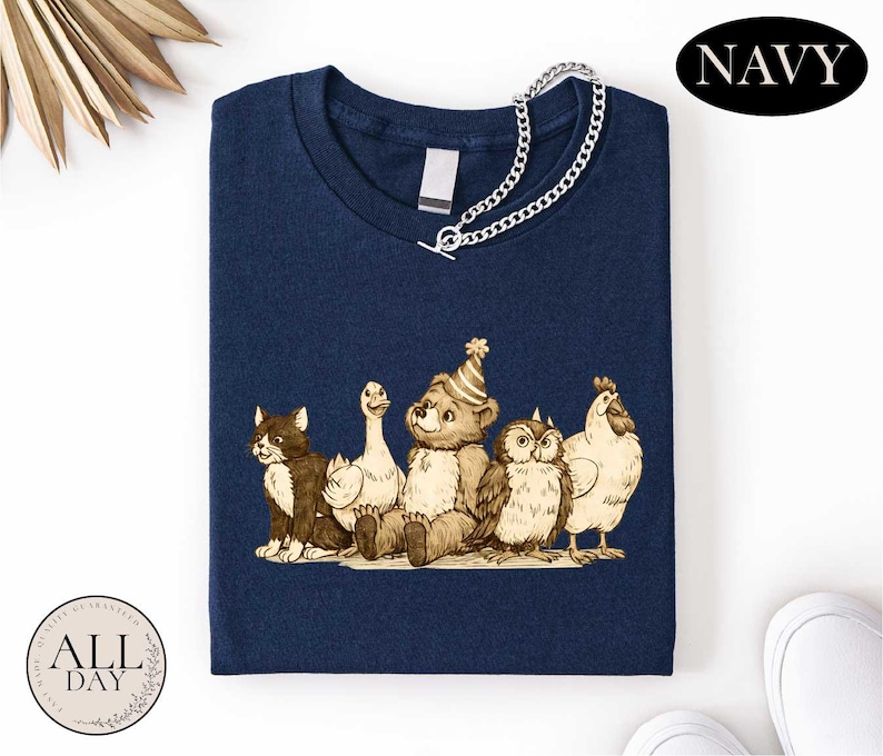 A navy blue t-shirt with a graphic design depicting a group of animals, including a bear, cat, duck, chicken, and owl, all wearing party hats.