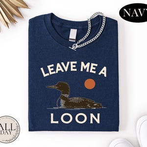 a navy blue t-shirt with a graphic design of a duck and the text "LEAVE ME A LON" printed on it.