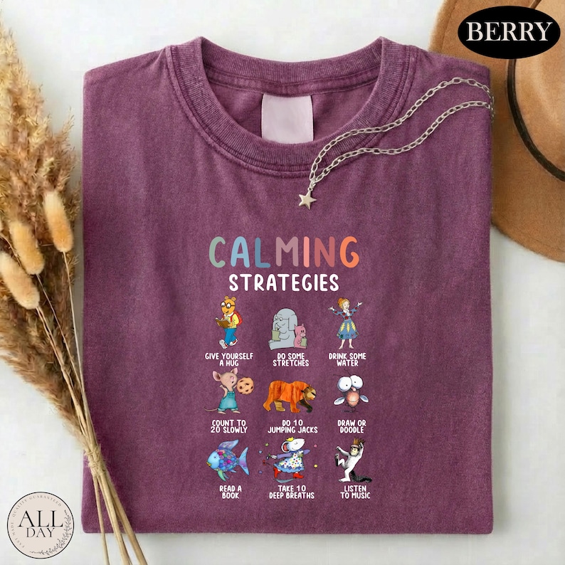 A purple t-shirt with a graphic design of various calming strategies and illustrations, including a dog, a cat, a bird, and a fish, along with text that describes each strategy.
