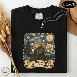 May include: A black t-shirt featuring a graphic of a black cat wearing a straw hat, holding a sign that reads NO ICE with a prohibition symbol over ice cubes. The background is a swirling starry night sky. The text NO ICE IN MY STARRY NIGHT is below.
