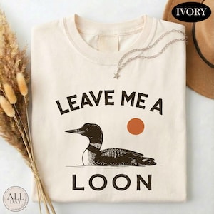 a white t-shirt with a graphic design of a duck and the text "LEAVE ME A LON" printed on it.