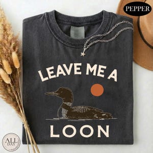 a black t-shirt with a graphic design of a duck and the text "LEAVE ME A LON" printed on it.