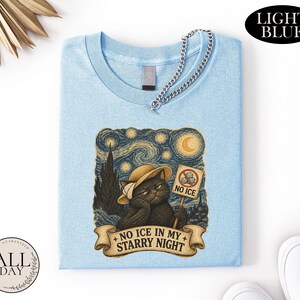 May include: A light blue t-shirt featuring a graphic of a black cat wearing a straw hat, holding a sign that says NO ICE with a crossed-out ice cube icon. Below the cat, a banner displays the text NO ICE IN MY STARRY NIGHT in dark lettering.