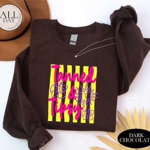 a brown t-shirt with a graphic design, a brown hat, and some decorative leaves, all placed on a white background.