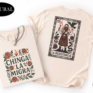 May include: Two cream-colored t-shirts. One features the text "CHINGA LA MIGRA" surrounded by roses and leaves. The other displays a graphic of a woman with a torch, a bird, and a snake, with the words "LA RESISTENCIA".