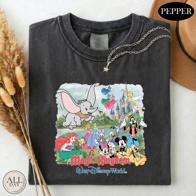 A black t-shirt with a graphic design depicting various Disney characters from the Magic Kingdom, including Dumbo, Minnie Mouse, Mickey Mouse, Donald Duck, and other iconic figures.