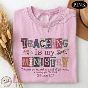 May include: Pink t-shirt with the text "TEACHING is my MINISTRY" in colorful block letters. The shirt also features the Bible verse Colossians 3:23. A silver necklace with a star pendant is draped on the shirt.