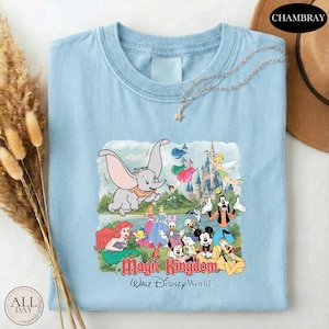 A light blue t-shirt with a Disney-themed graphic of characters from the Magic Kingdom, including Dumbo, Minnie Mouse, Mickey Mouse, Donald Duck, and other iconic Disney characters, along with a castle and a star.
