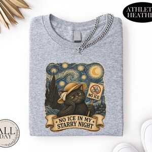 May include: An athletic heather gray t-shirt featuring a graphic of a black cat wearing a straw hat. The cat holds a sign that says NO ICE with a red circle and slash. Below the cat, a banner displays the text NO ICE IN MY STARRY NIGHT.