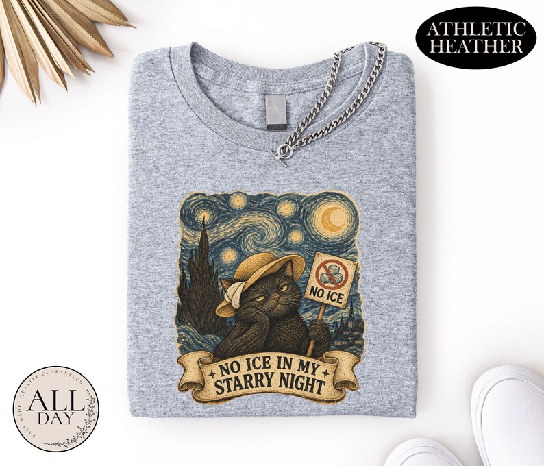 May include: An athletic heather gray t-shirt featuring a graphic of a black cat wearing a straw hat. The cat holds a sign that says NO ICE with a red circle and slash. Below the cat, a banner displays the text NO ICE IN MY STARRY NIGHT.