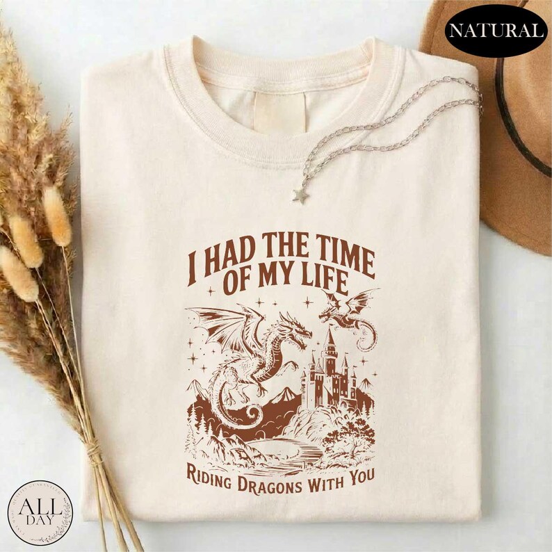 a white t-shirt with a graphic design depicting a dragon and a castle, along with the text "I HAD THE TIME OF MY LIFE RIDING DRagons WITH YOU".