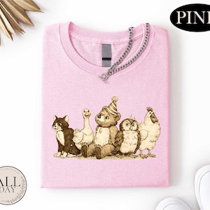 A pink t-shirt with a cartoon illustration of a bear, cat, duck, chicken, and owl wearing party hats.