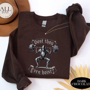 A brown t-shirt with a graphic design depicting a knight lifting a barbell, accompanied by the text "Post thou Even hoist?"